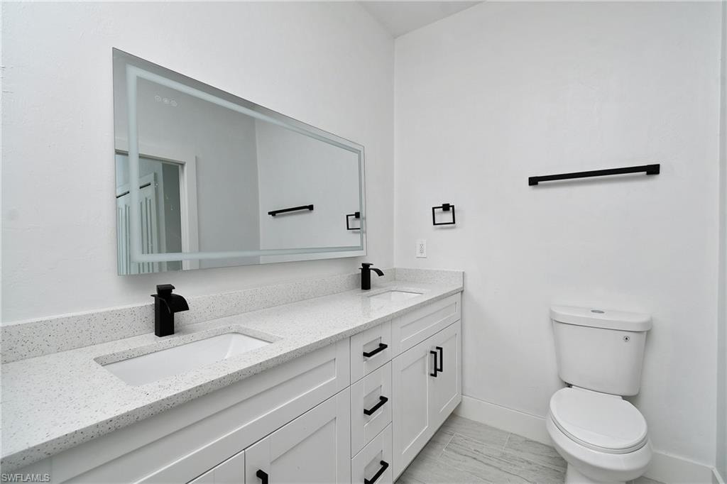 Double vanity with integrated sinks, speckled countertop, white cabinetry with black hardware, back-lit vanity mirror, and modern black fixtures