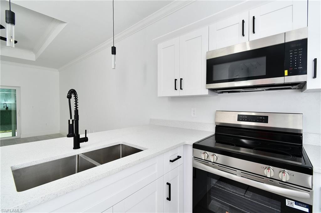 White shaker cabinetry with black hardware, stainless steel appliances, dual basin undermount sink with a black gooseneck faucet, and light-toned countertops