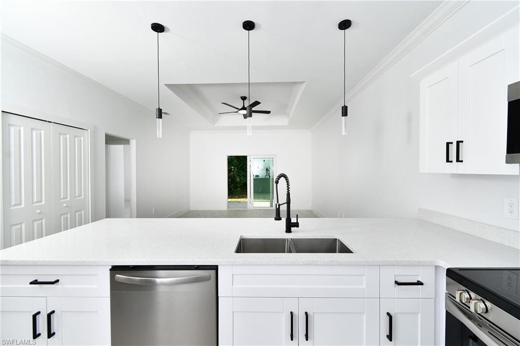 White shaker cabinetry with black hardware, stainless steel appliances, dual-basin sink with gooseneck faucet, light-toned countertops, and recessed ceiling with a fan