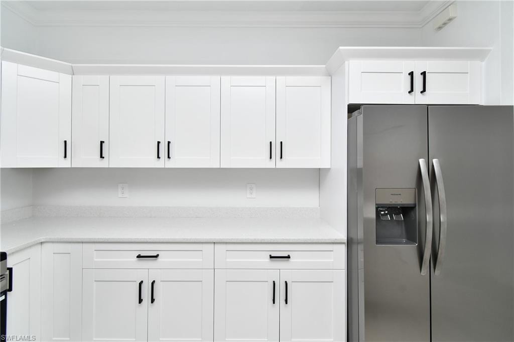 White shaker-style cabinetry with matte black hardware, light-toned countertops, and a built-in stainless steel refrigerator