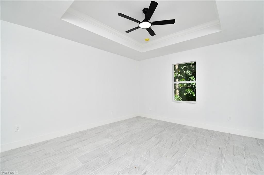 Recessed ceiling with crown molding, ceiling fan with integrated lighting, window with exterior greenery, and light-toned tile flooring