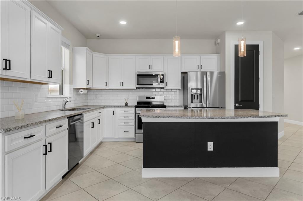Kitchen featuring white cabinetry, stainless steel appliances, speckled countertops, a subway tile backsplash, and an island with pendant lighting