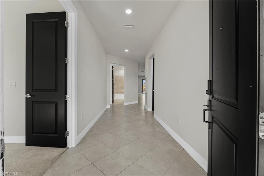 Hallway with large format tile flooring, recessed lighting, and contrasting dark paneled doors