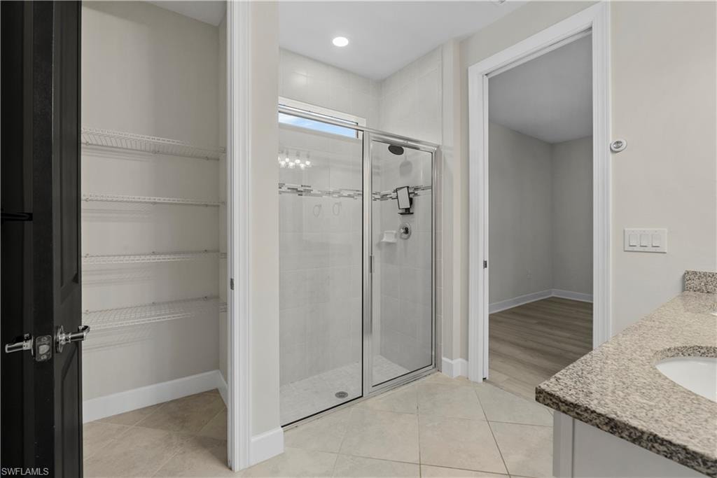 Glass-enclosed shower with tile surround, recessed lighting, tile flooring, and a vanity with a granite countertop and integrated sink