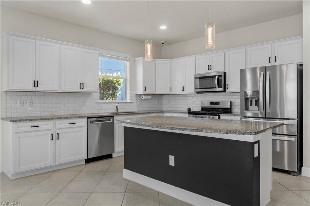 White cabinetry with black hardware, stainless steel appliances, granite countertops, subway tile backsplash, and tile flooring