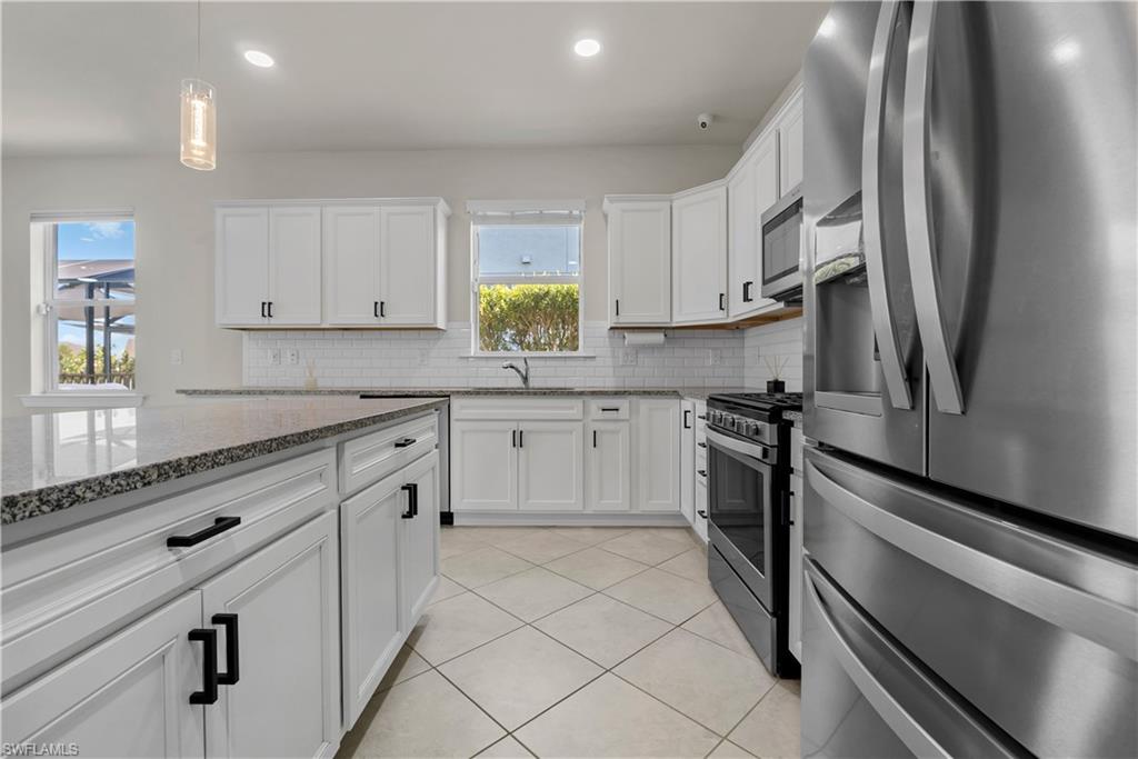 White cabinetry, tile flooring, stainless steel appliances, granite countertops, and subway tile backsplash