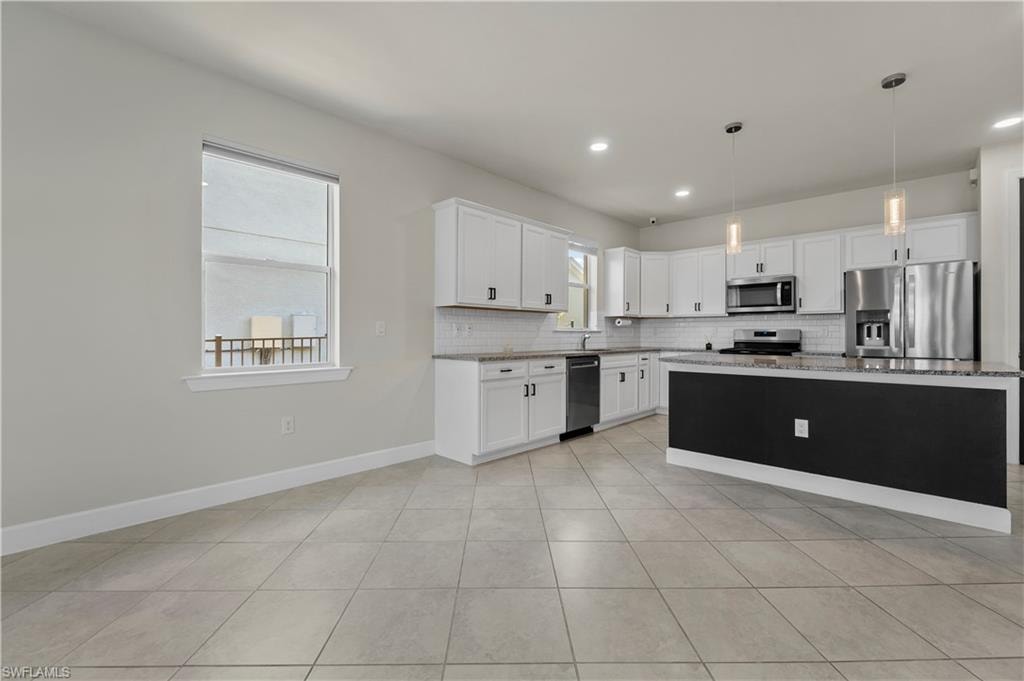 Open-concept kitchen featuring white cabinetry, dark island with contrasting countertop, stainless steel appliances, and tile flooring