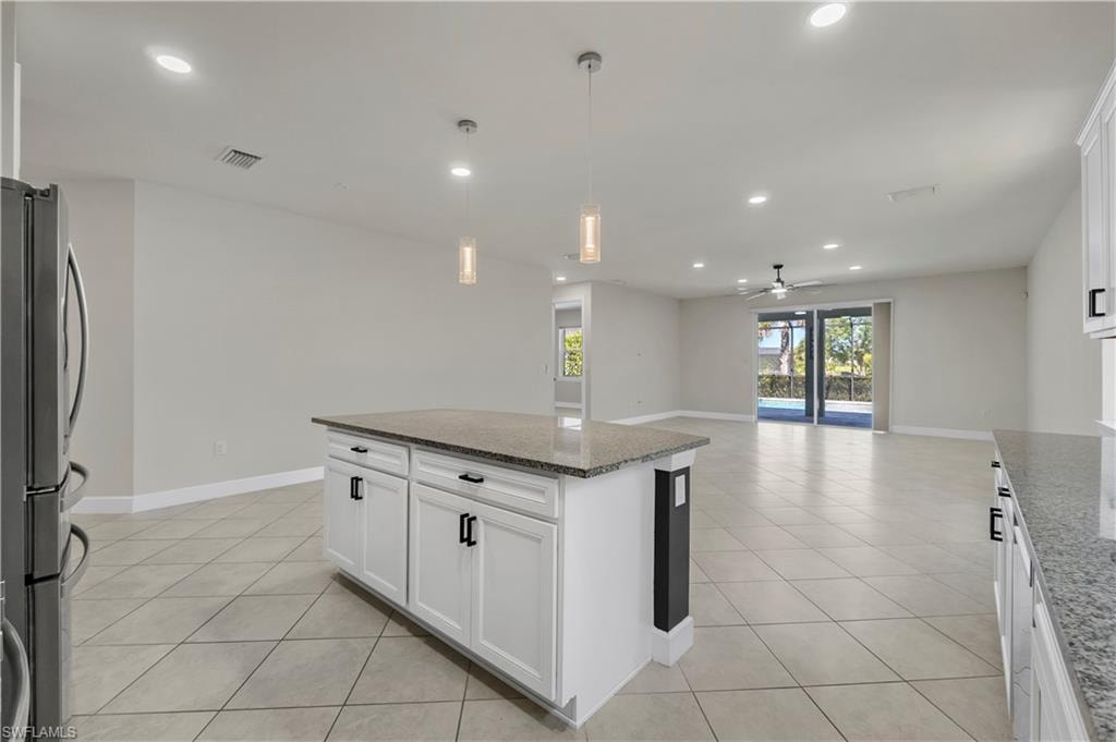 Kitchen island with white cabinetry and granite countertop, stainless steel refrigerator, tile flooring, recessed lighting, and patio doors