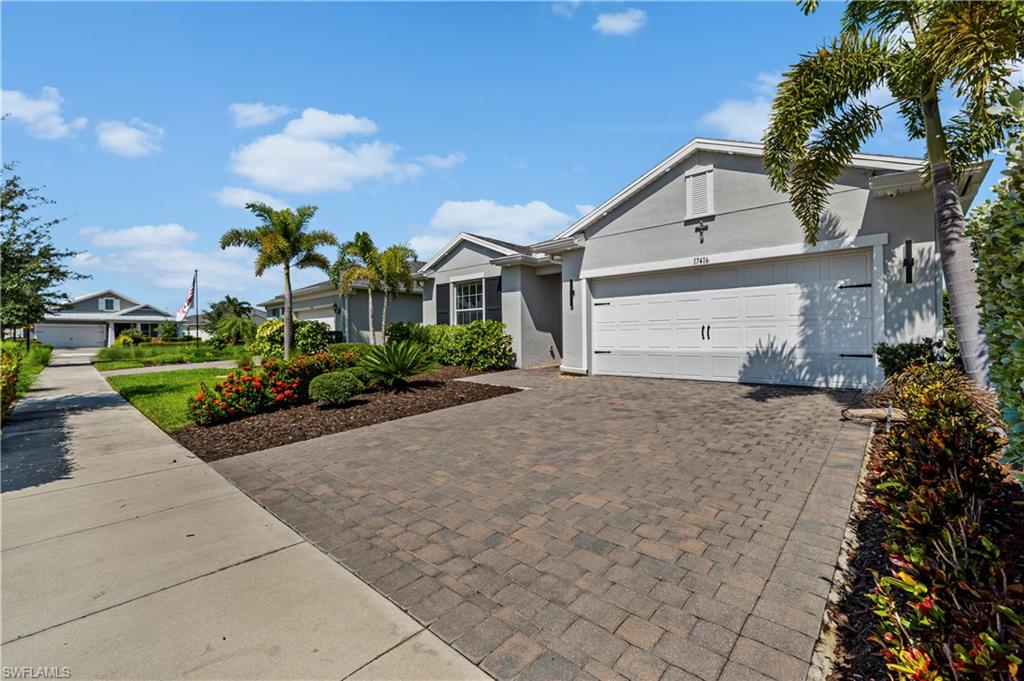 Paver driveway, mature palm trees, attached garage, well-maintained landscaping, and stucco exterior