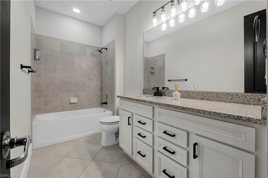 White vanity with dark hardware, stone-finish countertop, and large mirror