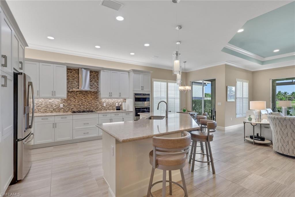 Kitchen featuring light-finish cabinetry, stainless steel appliances, a tile backsplash, and a large island with seating