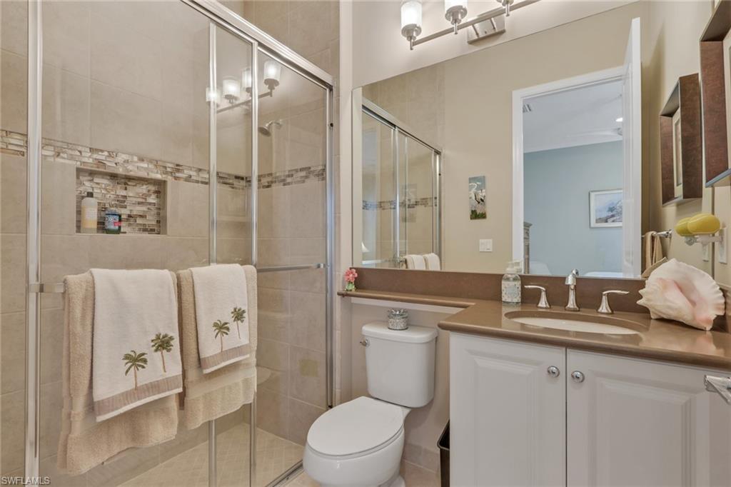 Spa-inspired ensuite bathroom featuring a frameless glass-enclosed shower with tile surround, dual-sink vanity with wood-finish countertop and white cabinetry, ceramic tile flooring, and large illuminated mirror