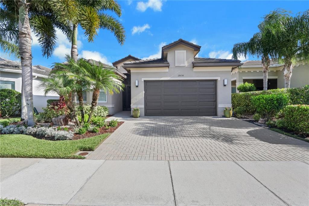 Stucco exterior with a paver driveway, mature landscaping, and a two-car garage