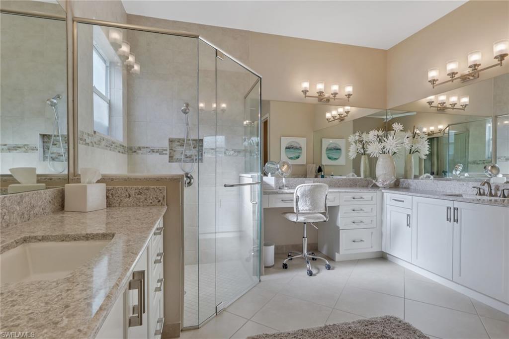 Dual vanities with integrated sinks and granite countertops, a built-in makeup vanity, a spacious glass-enclosed shower, and extensive mirror coverage