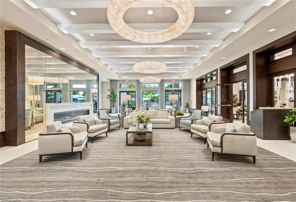 Spacious interior featuring multiple seating arrangements, two large circular chandeliers, an elongated fireplace, and wood-paneled accents