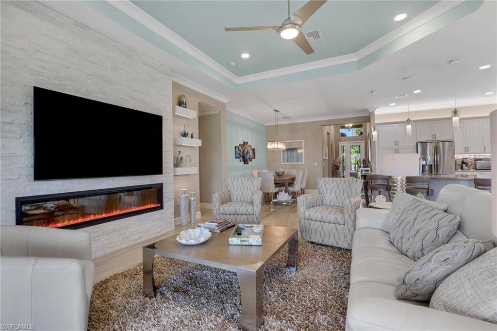 Integrated electric fireplace with a stacked stone wall surround, tray ceiling with a ceiling fan, recessed lighting, and built-in shelving