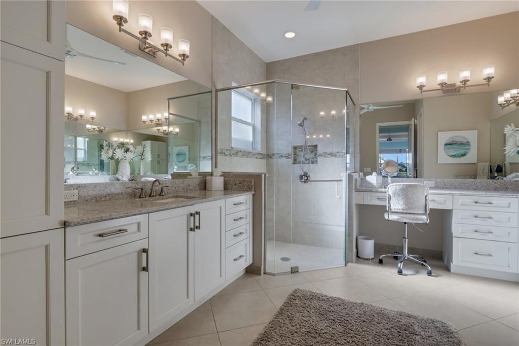 Dual vanities with granite countertops, custom cabinetry, large walk-in shower with tiled walls, and tiled flooring