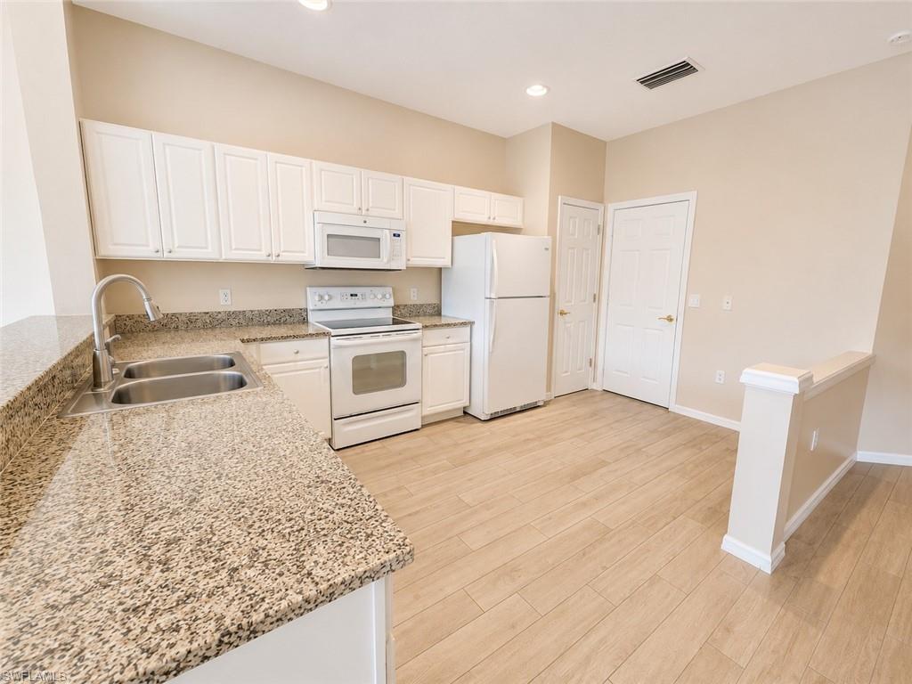 Kitchen featuring white cabinetry, light-toned countertops, a double basin stainless steel sink, and wood-finish flooring