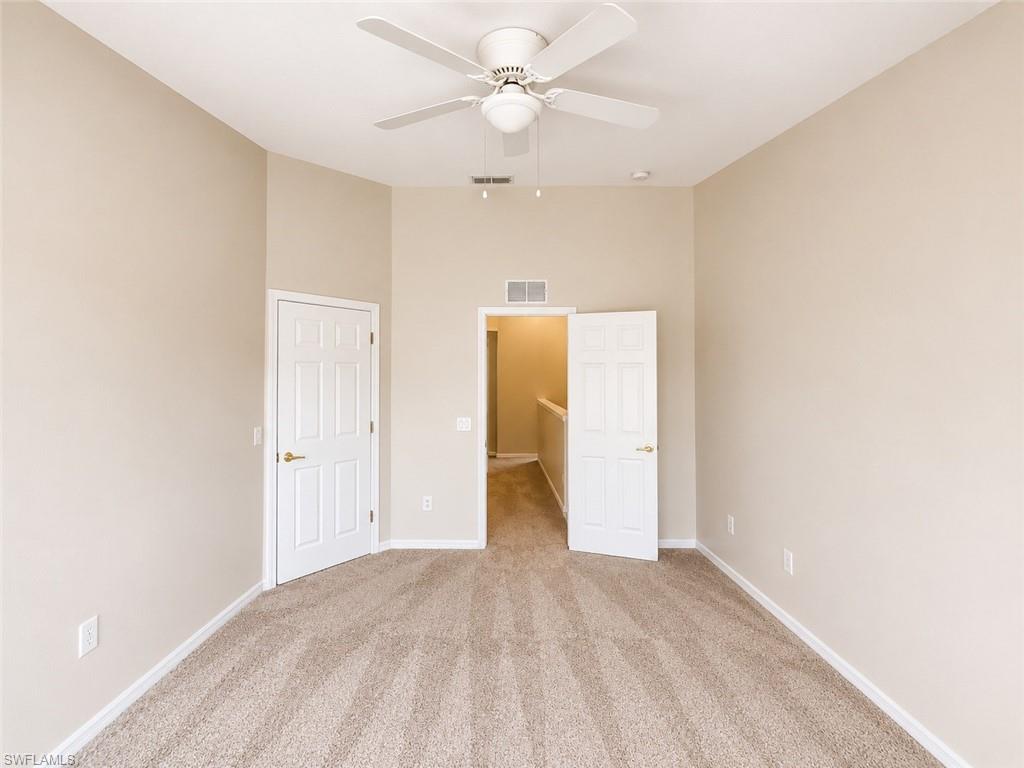 Neutral tone wall paint with vaulted ceiling, textured carpeting, and a ceiling fan with integrated lighting