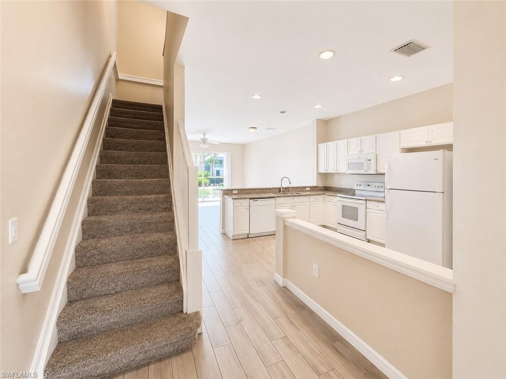 Kitchen featuring wood-finish flooring, white cabinetry, granite countertops, and white appliances