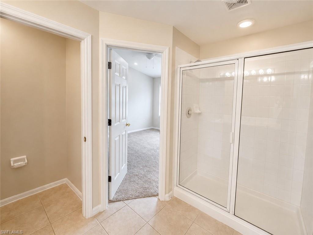Tiled flooring, glass-enclosed shower with white subway tile, recessed lighting, and a paneled interior door