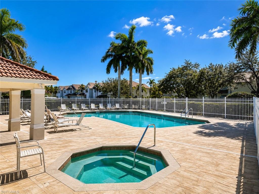 Fenced outdoor swimming pool with an integrated spa, surrounded by a paver deck and covered patio