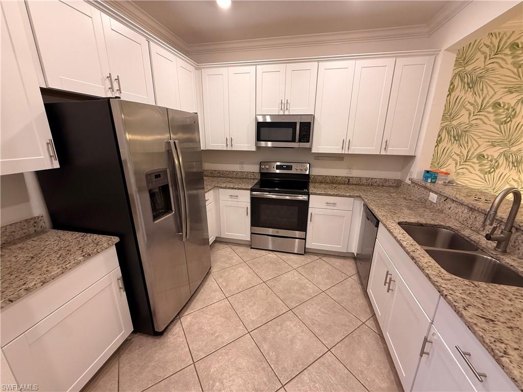 White shaker cabinetry, stainless steel appliances, dual basin sink, light-toned granite countertops, and tiled flooring