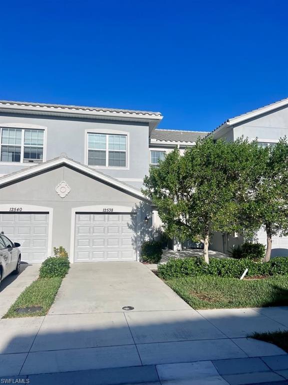 Stucco exterior with multiple windows, two garage doors, concrete driveway, and front landscaping