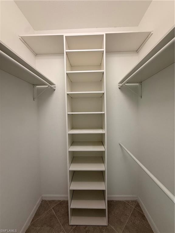 Walk-in closet with built-in shelving, hanging rods, and tile flooring