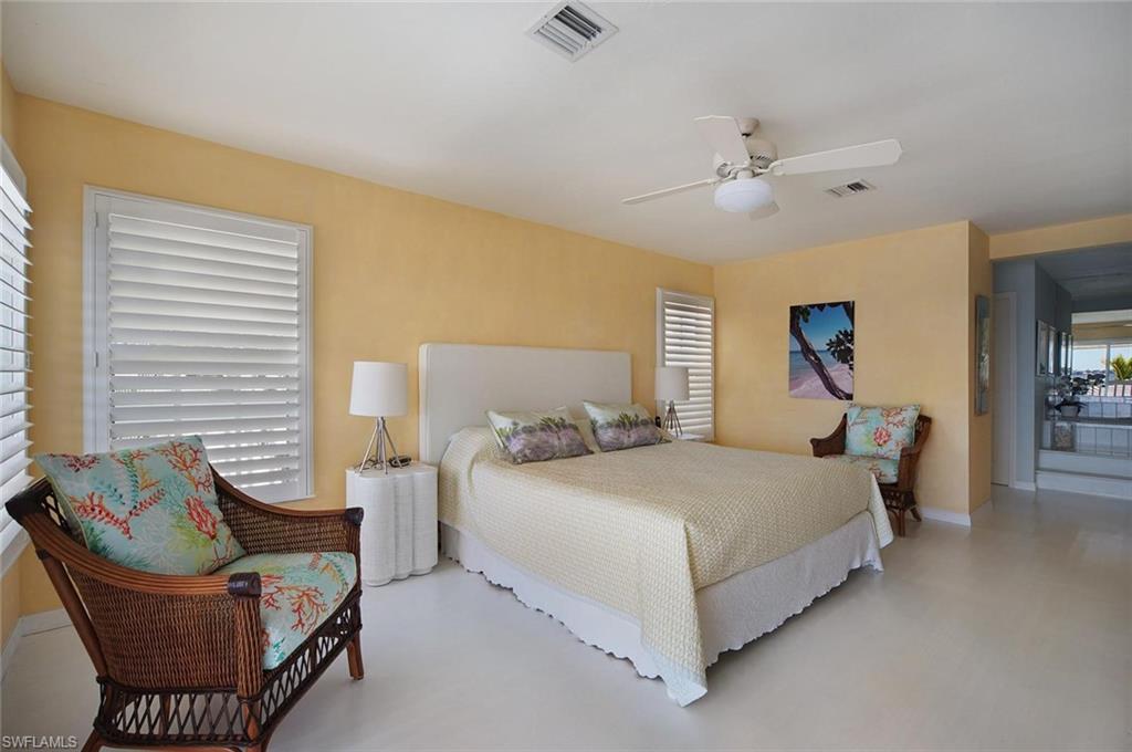 Spacious bedroom featuring light-toned flooring, white plantation shutters, and a ceiling fan with integrated lighting