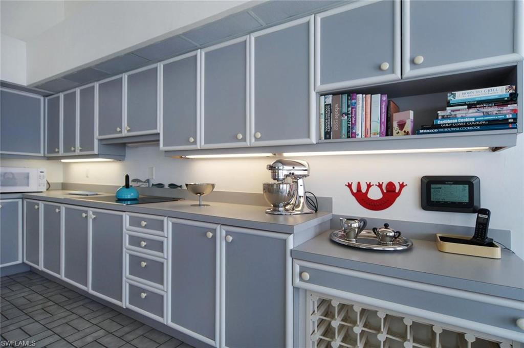 Kitchen featuring extensive grey cabinetry with white trim, solid surface countertops, and under-cabinet lighting