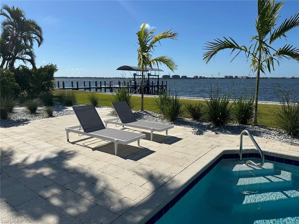 Waterfront property featuring a paver patio surrounding a pool, mature palm trees, a manicured lawn, and a private dock
