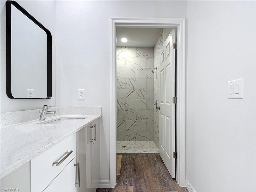 Bathroom featuring a marble finish shower, vanity, and dark wood-style flooring