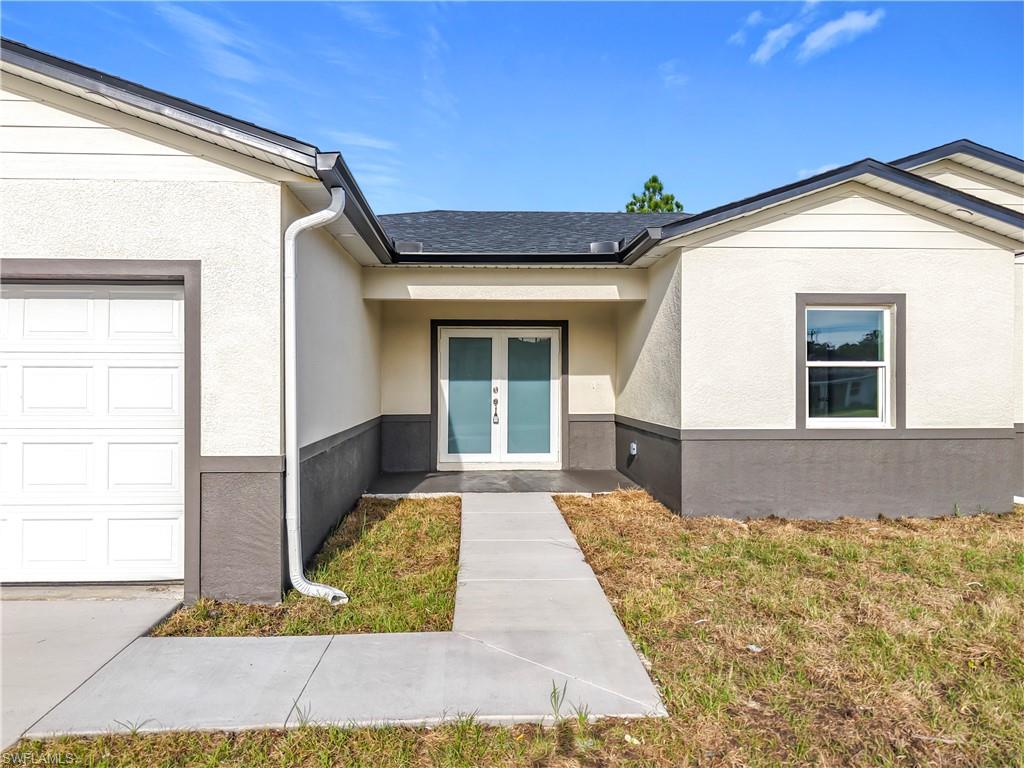 Property entrance featuring stucco siding, french doors, a garage, and a lawn