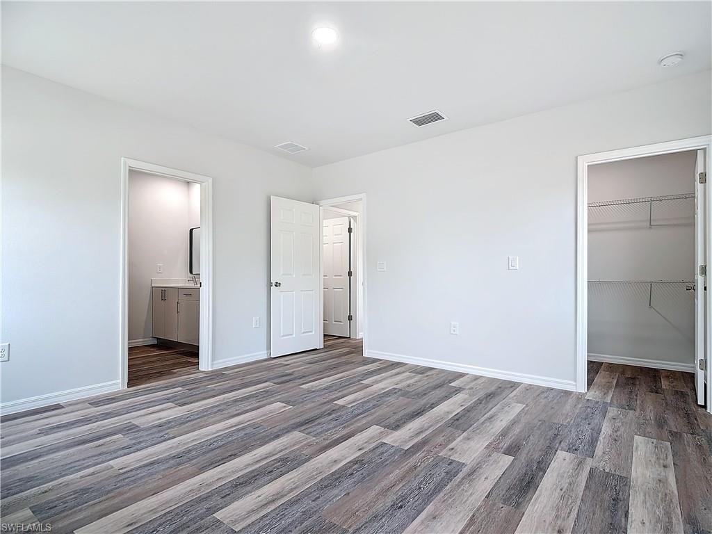 Unfurnished bedroom with wood finished floors, a spacious closet, and ensuite bathroom