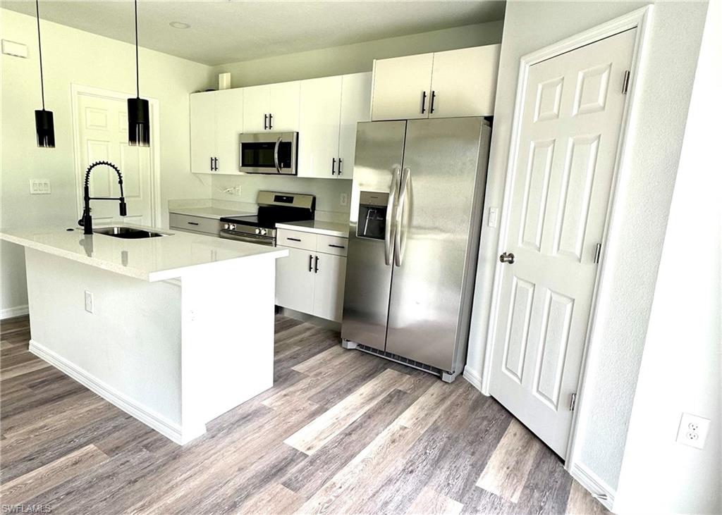 Kitchen featuring appliances with stainless steel finishes, white cabinetry, a center island with sink, and hanging light fixtures