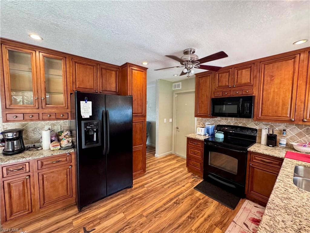 Kitchen featuring abundant wood-finish cabinetry, granite countertops, tile backsplash, wood-finish flooring, and a ceiling fan with integrated lighting