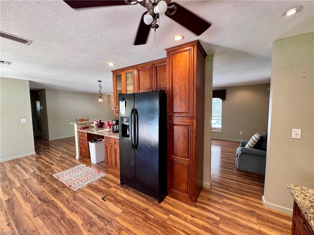 Kitchen featuring wood-finish flooring, recessed lighting, wood cabinetry, and a black refrigerator