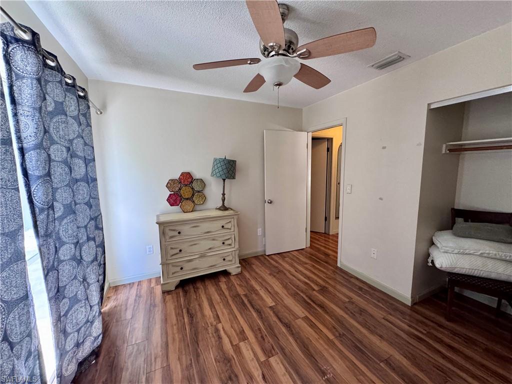 Wood-finish flooring, ceiling fan with integrated lighting, open doorway, and built-in closet with hanging rod