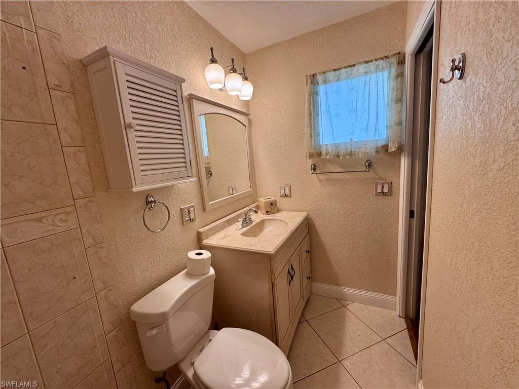 Integrated vanity with undermount sink and countertop, wall-mounted mirror, ceramic tile flooring, and a window with a towel rod below