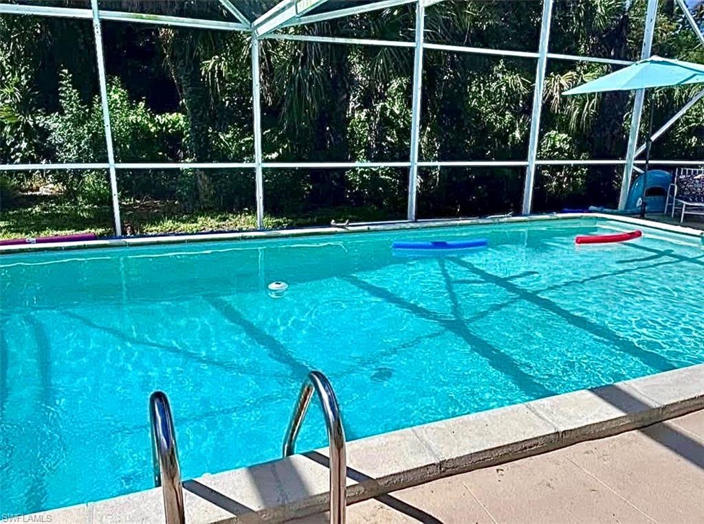 Screen-enclosed swimming pool with a bright blue interior finish, integrated steps, and surrounding deck paving
