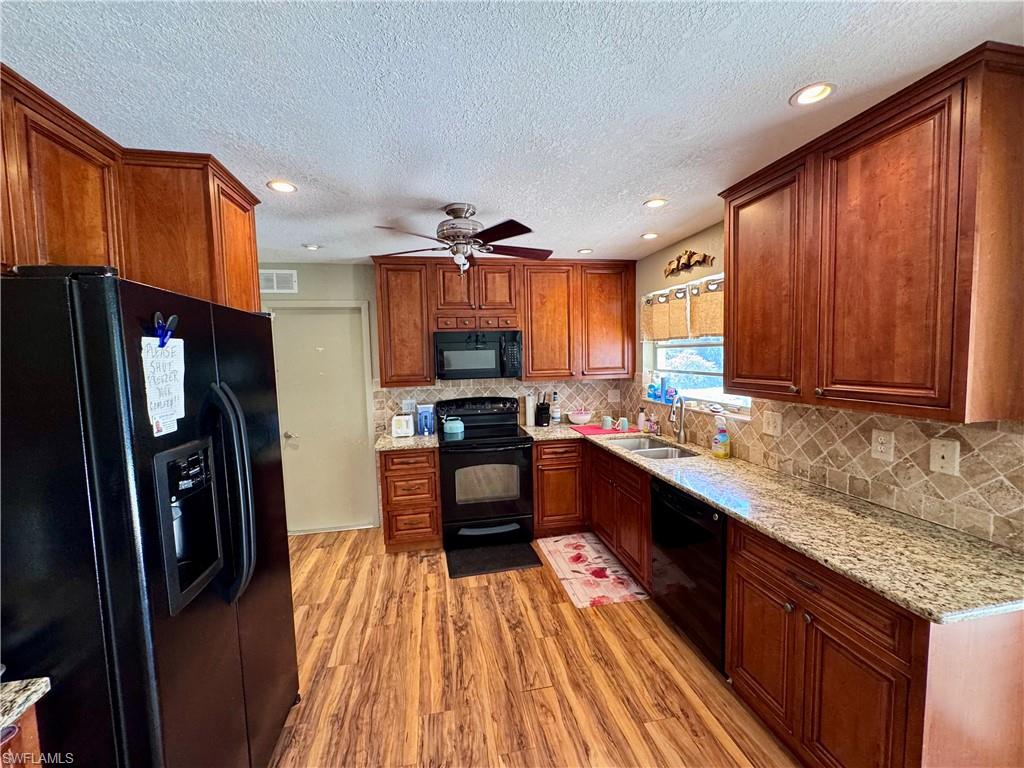 Kitchen featuring wood-finish flooring, wood cabinetry, granite countertops, and a tile backsplash