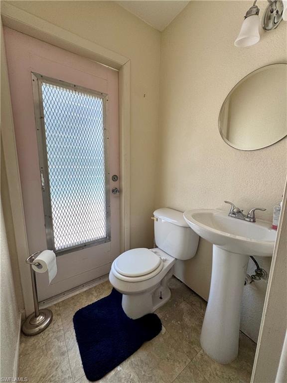 Bathroom featuring a pedestal sink, toilet, wall-mounted light fixture, and an oval mirror
