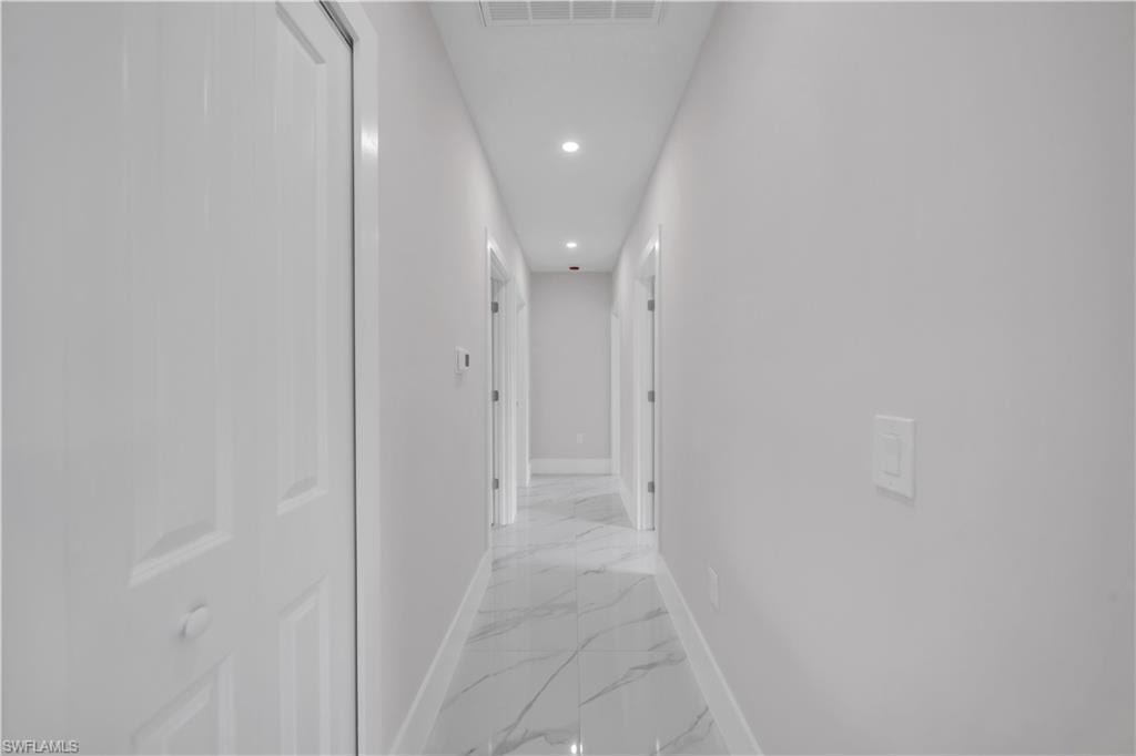 Recessed ceiling lighting illuminates a hallway with white walls and a large format tile floor