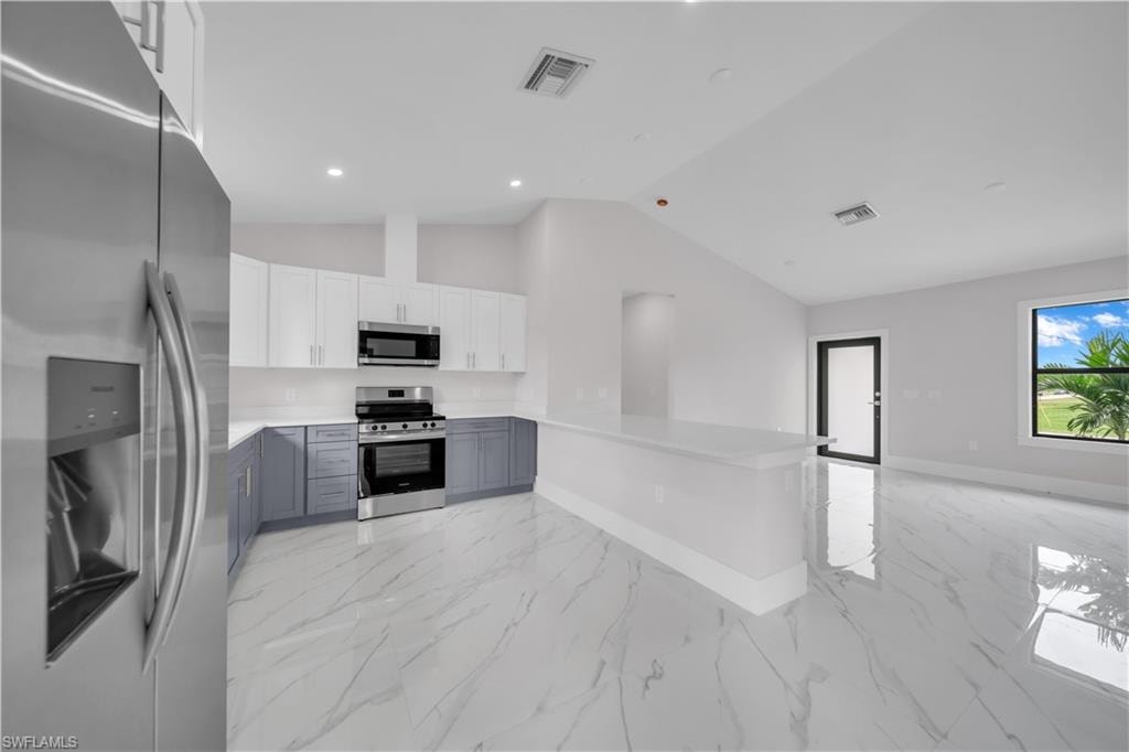 Open-concept living space with large format tile flooring, stainless steel appliances, white and gray cabinetry, and a spacious kitchen island