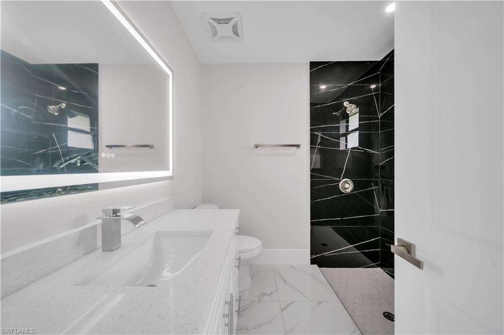 Walk-in shower with black tile surround, vanity with an integrated sink, illuminated mirror, and marble-look floor tile