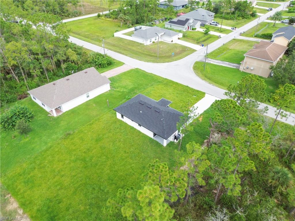 Expansive corner lot featuring a newly constructed residence with a dark shingle roof and white exterior, alongside a separate detached structure with a light shingle roof