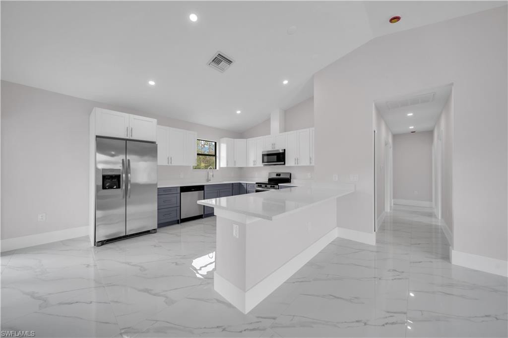 Kitchen featuring white and grey cabinetry, stainless steel appliances, a white countertop island, and tile flooring