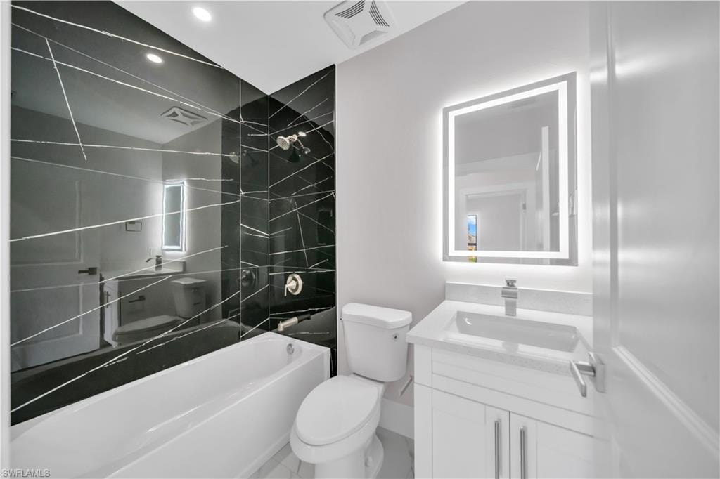 Black tiled shower surround, integrated bathtub, recessed lighting, and a white vanity with a rectangular sink