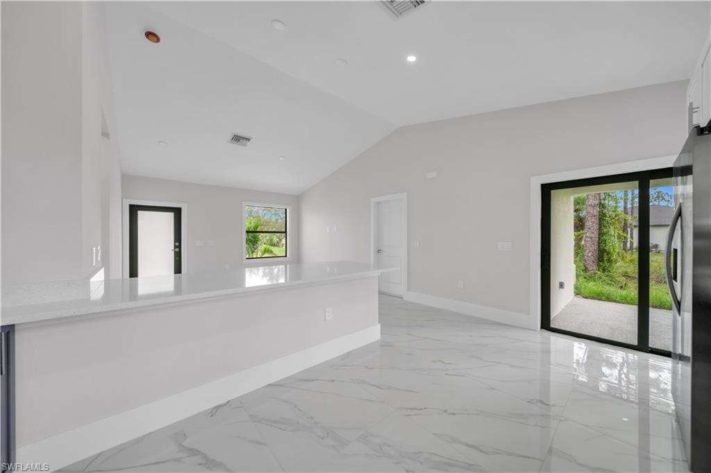 Vaulted ceiling, recessed lighting, white quartz countertop, large format tile flooring, and sliding glass doors to the exterior